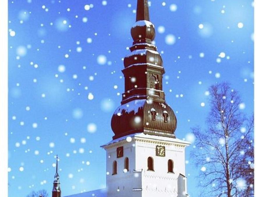 Stora Tuna kyrka i snö, en vit stor kyrka med ett svart torn.