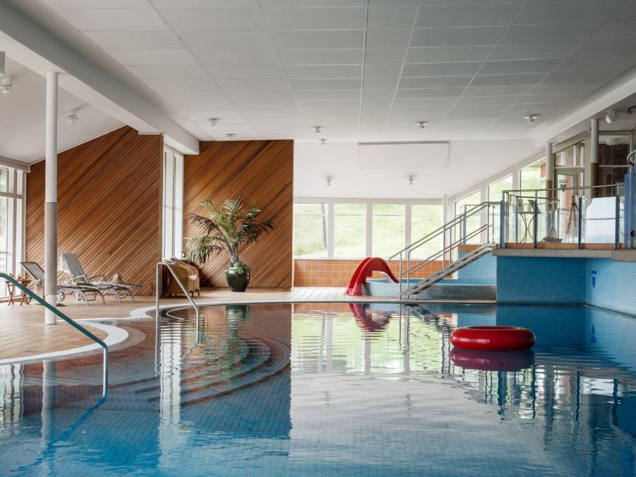 A swimming pool, a red bathing ring in the pool, sun loungers, children's pool and stairs in the background.