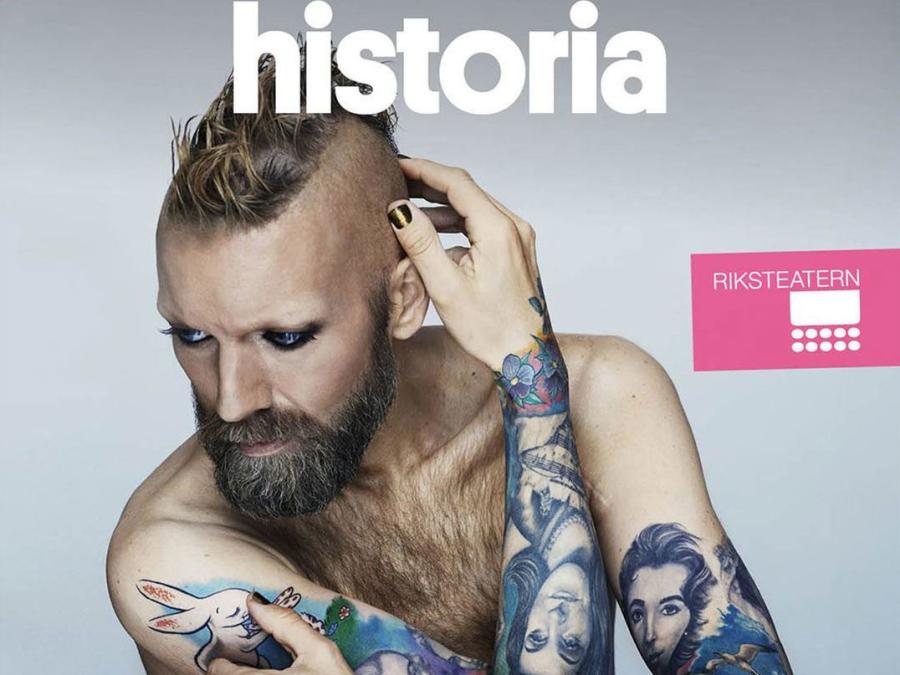 En man i bar överkropp, snaggat hår, skägg och tatuerade armar, text Kärlekens historia.