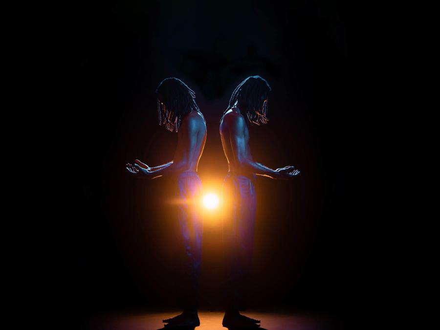 Två män med bara överkroppar står med ryggarna emot varandra, en lampa lyser i bakgrunden.