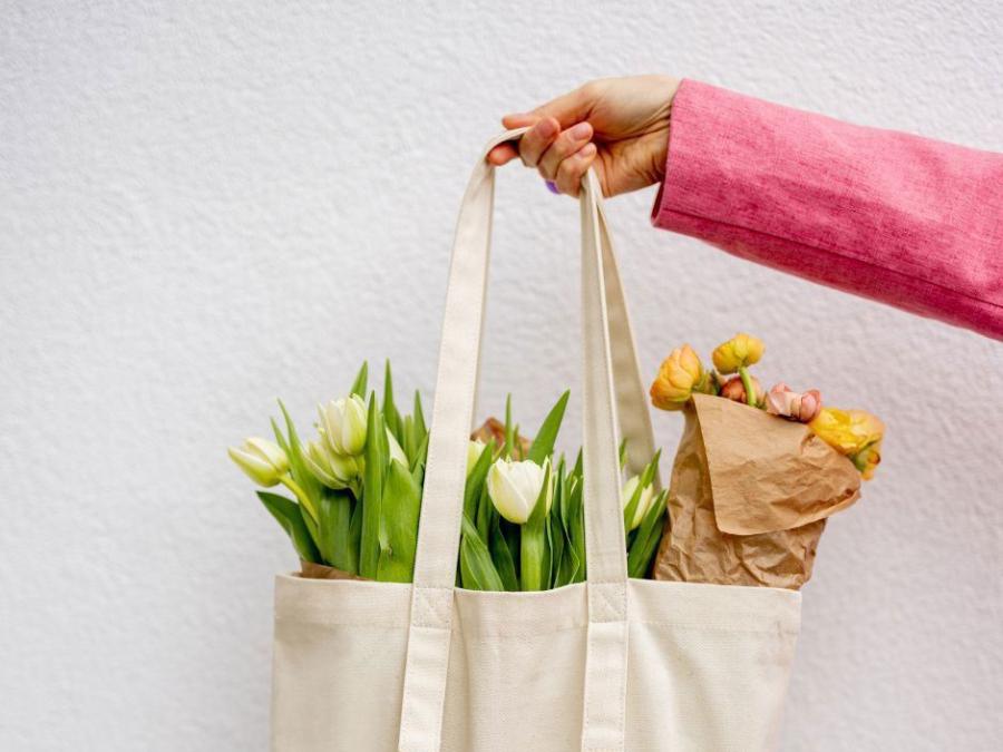En hand håller upp en vit väska med tulpaner i.