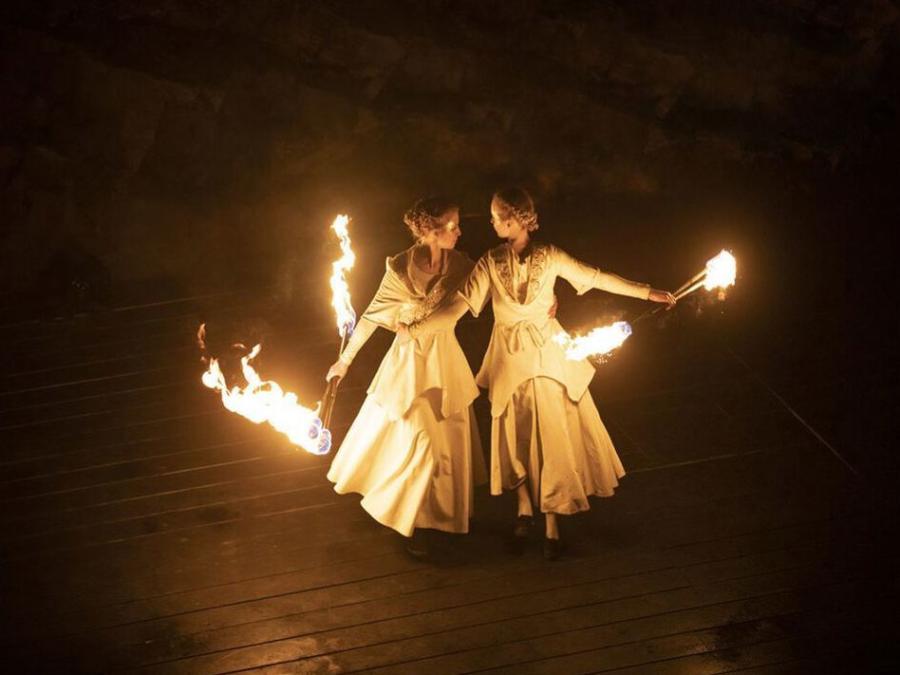 Två damer i vita klänningar som dansar med eld.