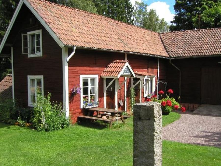 Red cottage with a table and benches in front of it.