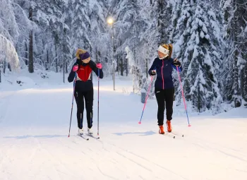 Två kvinliga längdskidåkare som åker i bredd i varsitt spår.