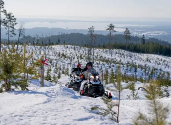 Skoteråkare på skotrar i snöigt landskap med vacker utsikt över landskapet.