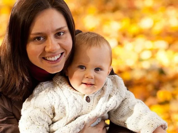 En mamma kikar fram bakom ett träd och lyfter sitt barn. 