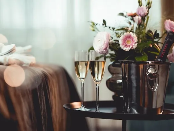 hotellsäng med blommor, vin och två vinglas på ett bord.