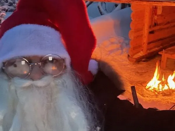 Tomten framför ett vindskydd med sprakande brasa.