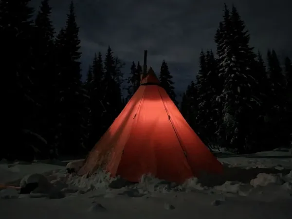 A teepee tent in the middle of the snow out in the forest.