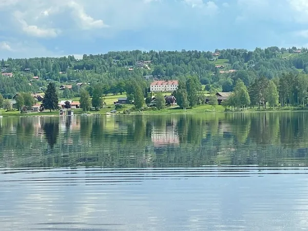 Ett hotell vid en spegelblank sjö med åkrar och träd runtom.