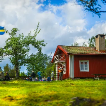 Rödmålad stuga med en flaggstång på gården.