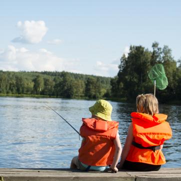 Två barn sitter på brygga och fiskar.