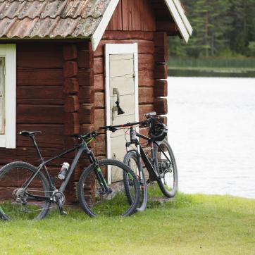 Two bicycles lined up against a house wall by a lake.
