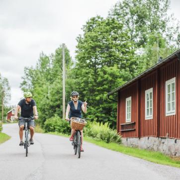 Två personer cyklar på liten väg i grönskande landskap.