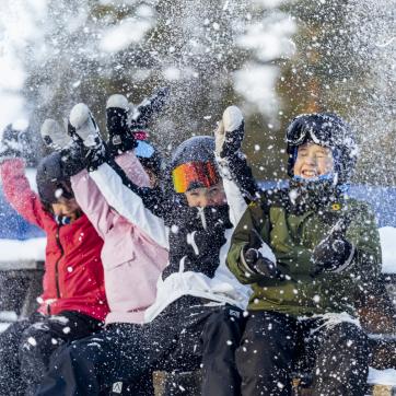 Fyra barn i skidkläder kastar upp snö i luften.