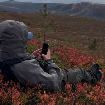 Kille som ligger och njuter på kalfjäll med sin mobil.
