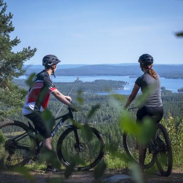 Två personer sitter på sina cyklar och blickar över utsikten efter en cykelled i skogen.