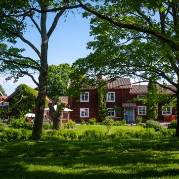 Gamla Byn i Avesta, röda äldre hus bland höga träd.