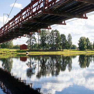 A long bridge is reflected in the water under a blue sky.