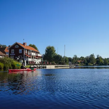 Ett rött hus speglas i blått vatten under blå himmel.