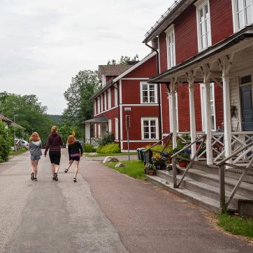 Two children and an adult walk along a street next to a red house.