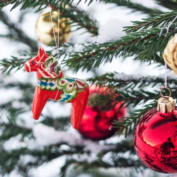 A dala horse and Christmas tree decorations hang on a tree.