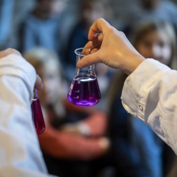 Barn håller upp provrör under kemishow på 2047 Science Center i Borlänge.
