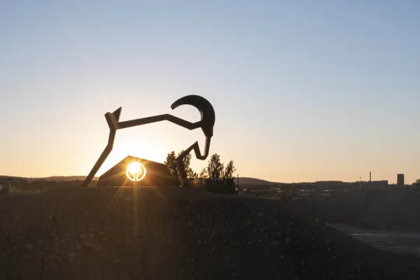 Copper statue of the Goat Kåre with sunset in the background.