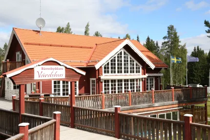 En röd träbyggnad med stora glaspartier, röd träportal med text Bäverhyddans värdshus.