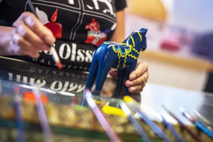 Krusmålare med pensel i handen målandes en blå dalahäst med krus.