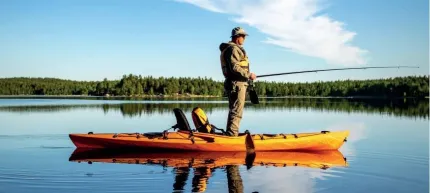 En person står i en orange kajak och fiskar på en spegelblank sjö med skog i bakgrunden och klar himmel.