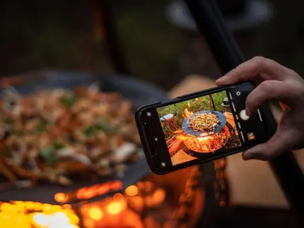 A mobile phone that zooms in on food being cooked over an open fire.