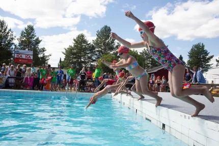 Barn som dyker ner i en pool, publik på sidan av poolen.