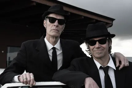 Två män i svarta hattar, vita skjortor, svart slips, svart kavaj och svarta solglasögon.