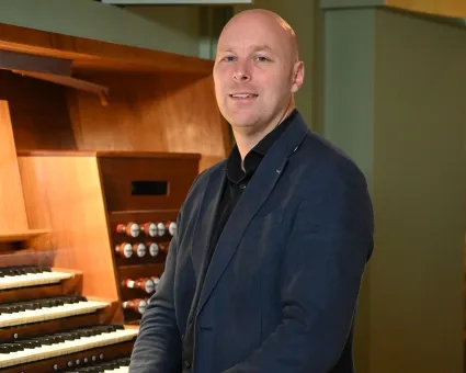 En man i blå kavaj och svart skjorta sitter framför en kyrkorgel.