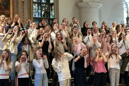 En grupp ungdommar i kyrkomiljö, de har händerna vid munnen och öppna munnar.