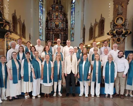En grupp män och kvinnor i ljusa kläder, kvinnorna med gröna sjalar, de står i en kyrka.