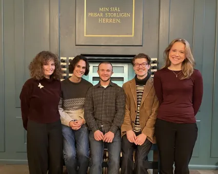 Tre unga män i mitten och två unga kvinnor på sidorna, grå panel i bakgrunden.