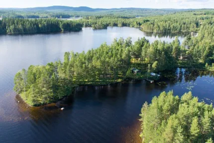 Bild från ovan över sjö med udde mitt i med tät skog.