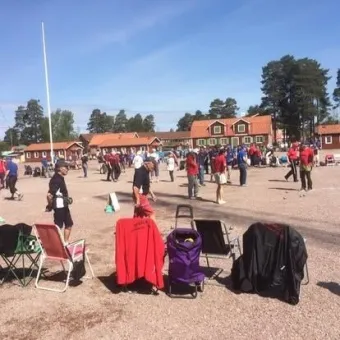 En öppen yta där människor samlats för att spela boule, stolar i framkant.