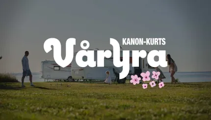 Husvagnar vid vatten, våryra med vita bokstäver, rosa animerade blommor, en man och en kvinna på varsin sida av husvagnen, gräsmatta i framkant.