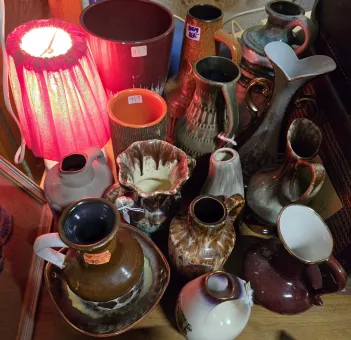 En röd bordslampa lyser över en samling keramikvaser, krukor och kannor på ett bord i ett inomhusutrymme..