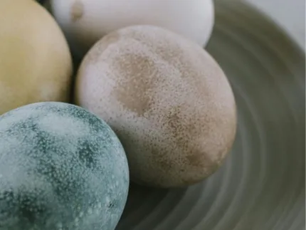 Närbild av flera pastellfärgade ägg med fläckig yta som ligger tätt tillsammans på en grå tallrik..