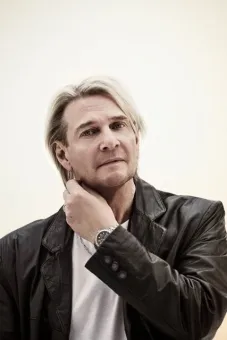 En man med blont hår iklädd svart skinjacka och vit t-shirt.