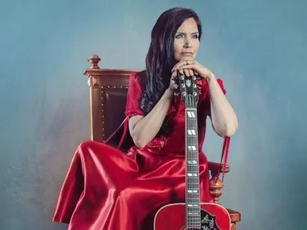 En person i en röd klänning sitter på en stol och håller i en gitarr.