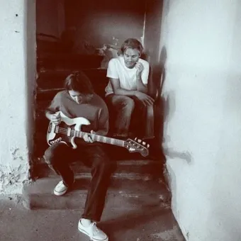 Två unga män som sitter i en trappa en av dem håller i en gitarr.