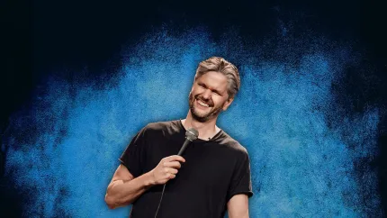En man i klädd svart t-shirt som håller i en mikrofon,  bakgrund i olika blå nyander.
