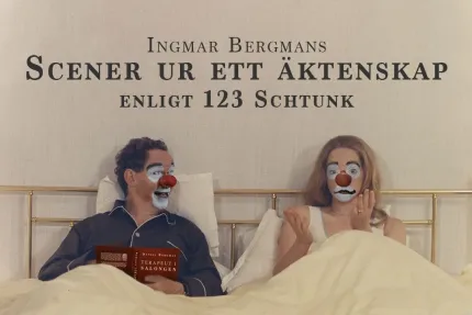 En man och en kvinna sitter i en säng med ljusa täcken; mannen håller en bok och kvinnan gestikulerar..