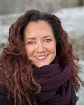 En kvinna med långt mörkt lockigt hår, en stor sjal virad om halsen.