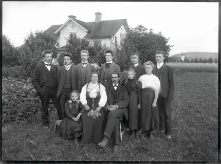 En svartvit bild på en familj med nio barn, alla i finkläder, bilden är från ca 1910.